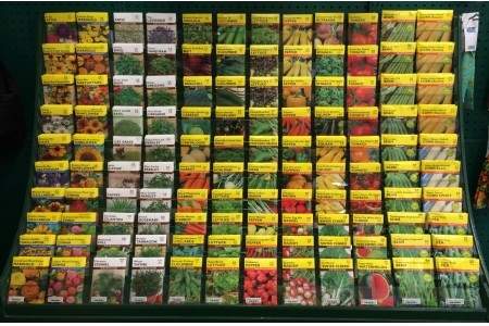 A display shelf filled with numerous packets of vegetable and flower seeds, each labeled with different plant names and colorful images of the plants they grow into.