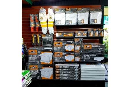 Display shelf with various beekeeping supplies including gloves, hive kits, and other accessories stacked and arranged neatly.